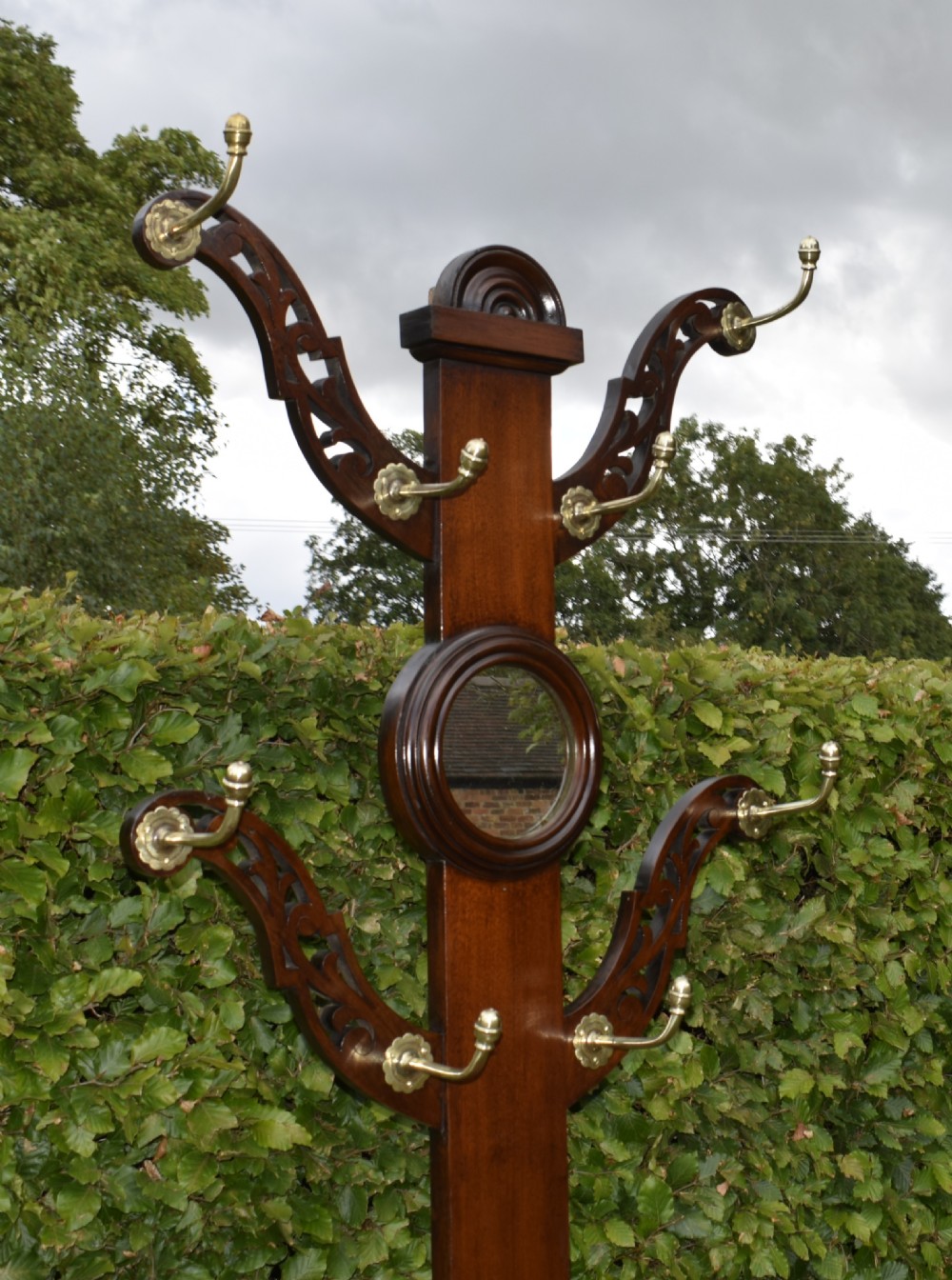 A Victorian walnut hall stand featuring carved fretwork branches, brass coat hooks, a central circular mirror, a glove box, and a lower drip tray base. View V