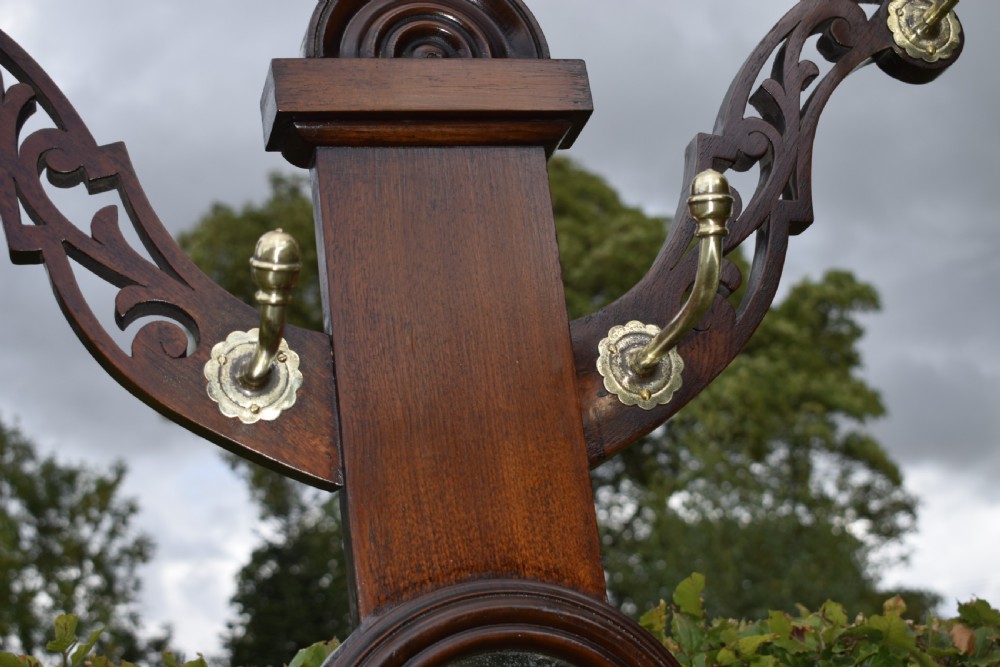 A Victorian walnut hall stand featuring carved fretwork branches, brass coat hooks, a central circular mirror, a glove box, and a lower drip tray base. View VIII