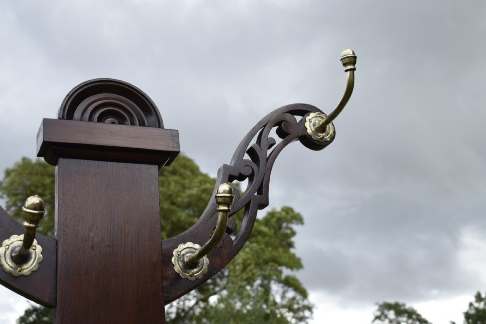A Victorian walnut hall stand featuring carved fretwork branches, brass coat hooks, a central circular mirror, a glove box, and a lower drip tray base. View IX