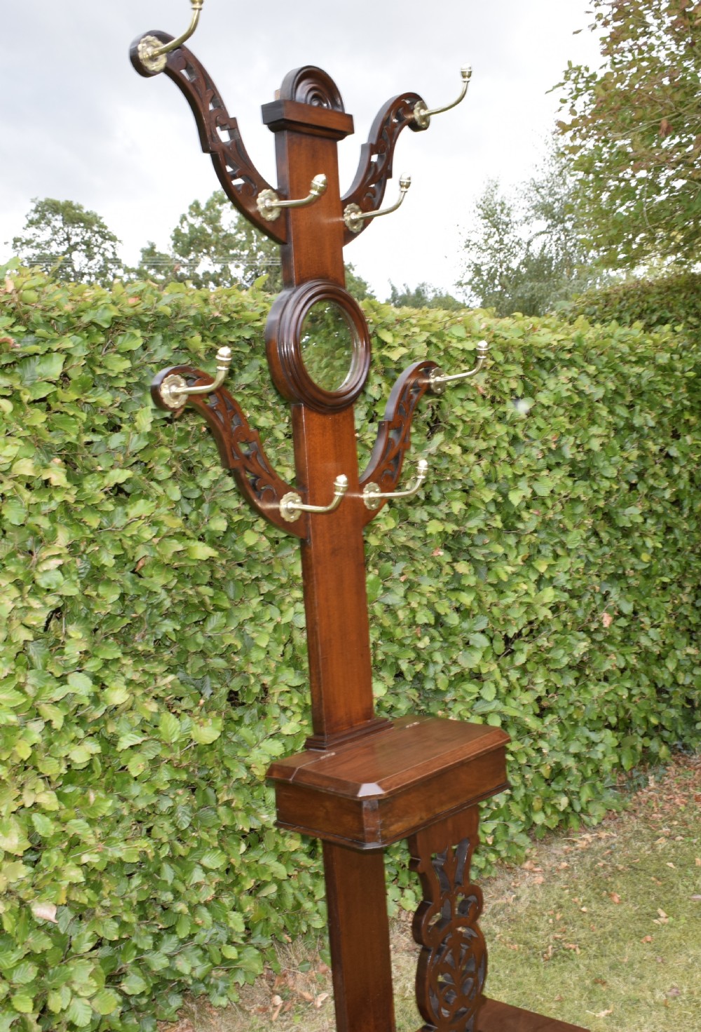 A Victorian walnut hall stand featuring carved fretwork branches, brass coat hooks, a central circular mirror, a glove box, and a lower drip tray base. View XIV