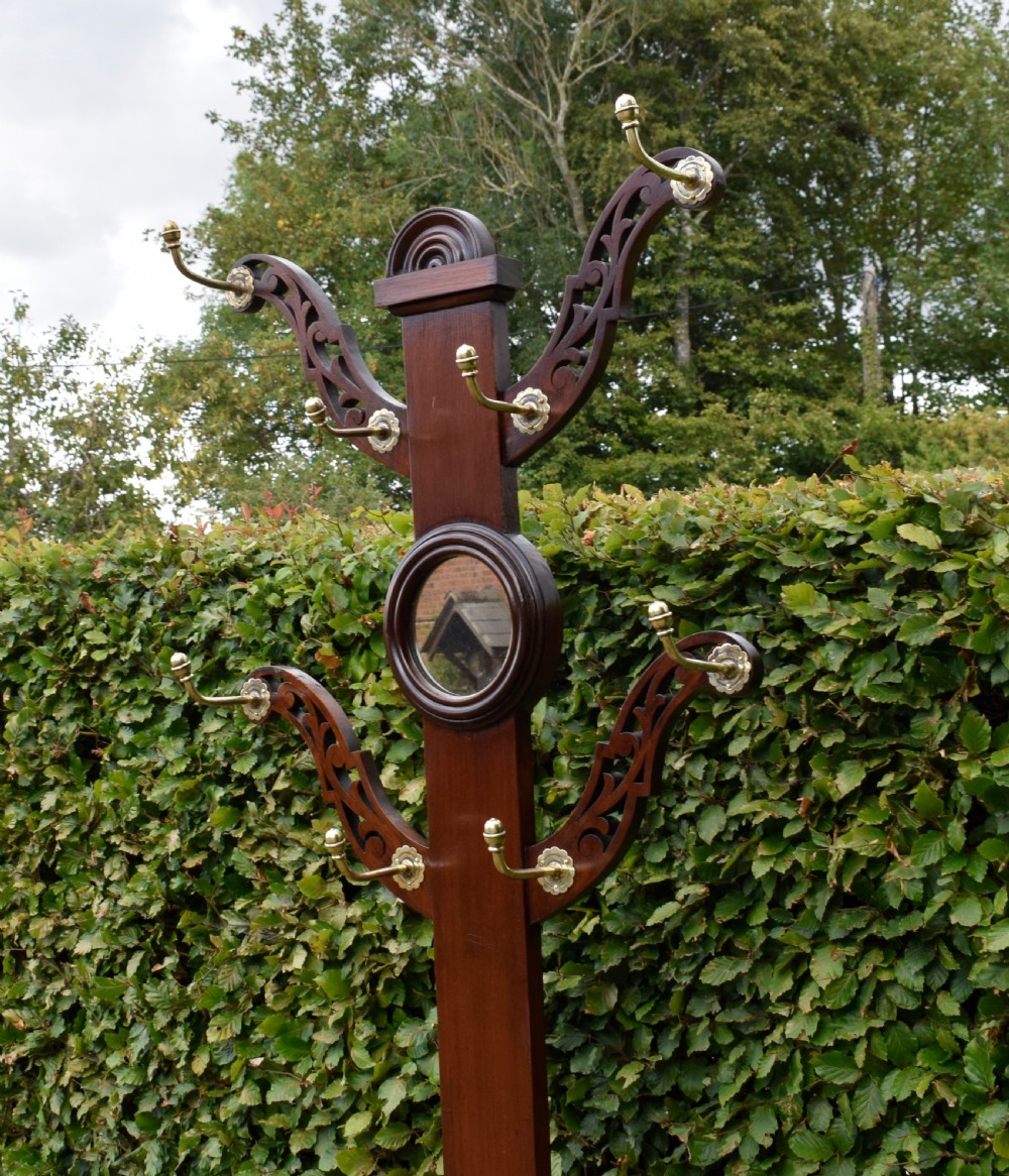A Victorian walnut hall stand featuring carved fretwork branches, brass coat hooks, a central circular mirror, a glove box, and a lower drip tray base. View XVIII