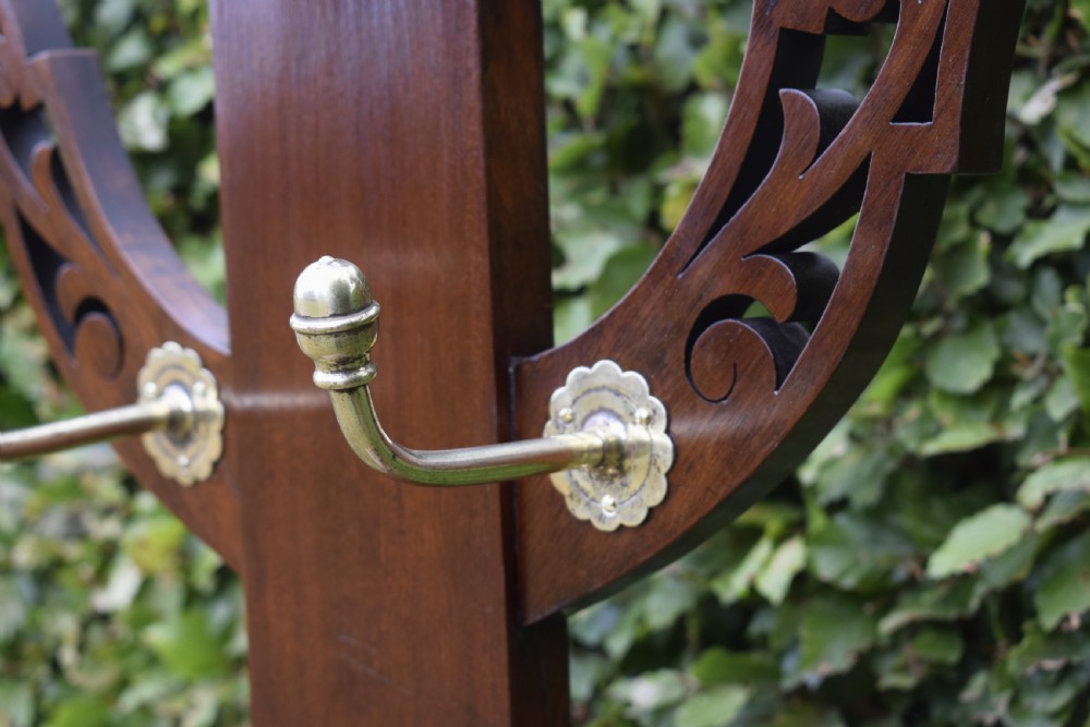 A Victorian walnut hall stand featuring carved fretwork branches, brass coat hooks, a central circular mirror, a glove box, and a lower drip tray base. View XIX