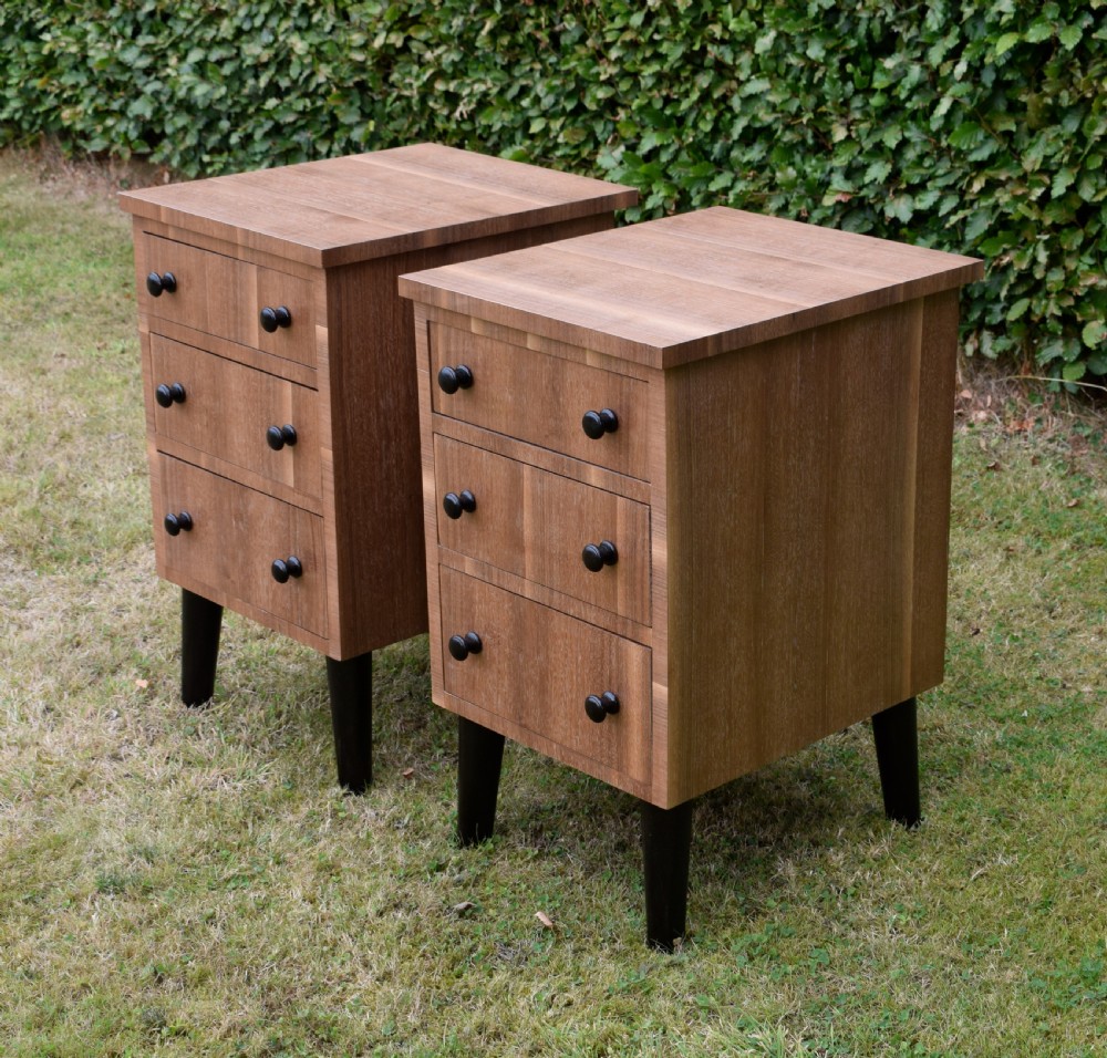 A matching pair of three-drawer walnut bedside chests featuring dark turned knobs and ebonised tapered legs.