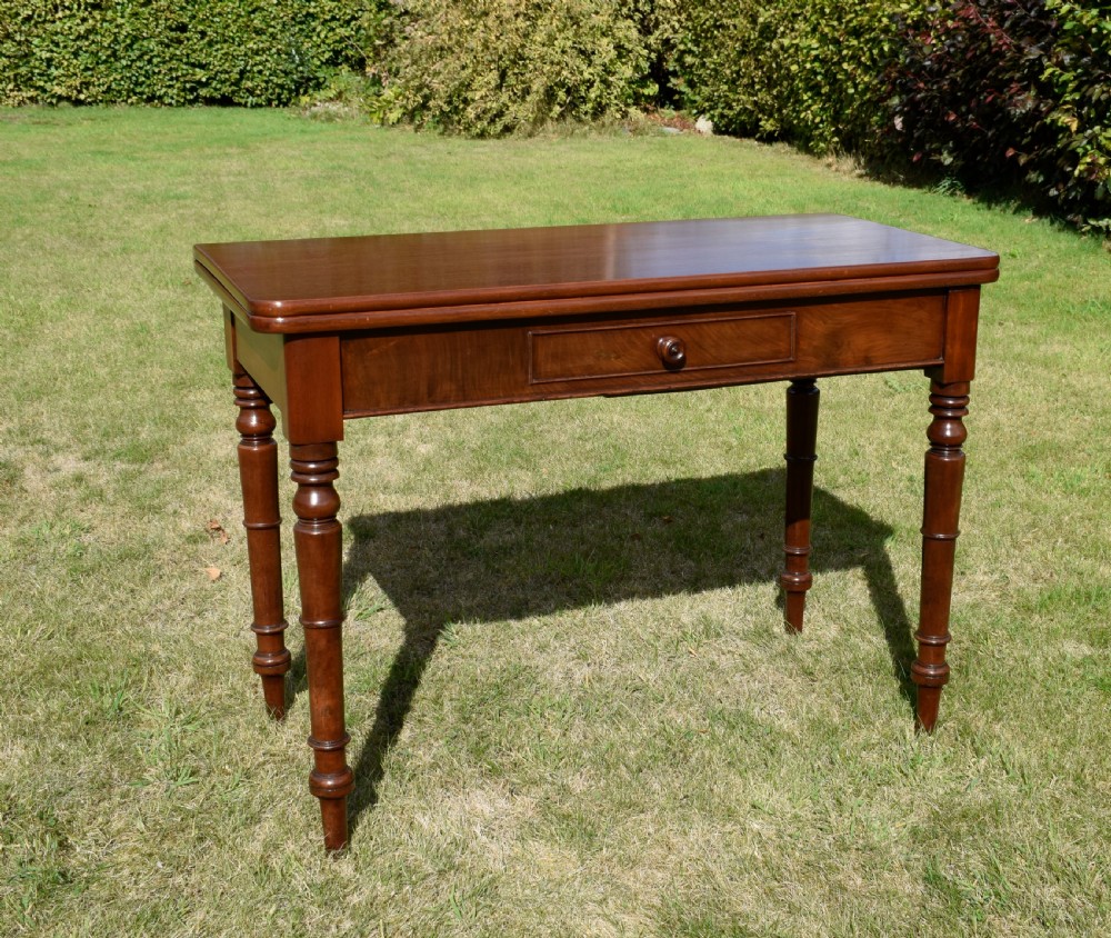 A William IV polished mahogany fold-over games table with turned legs and a single central drawer with a wooden knob.