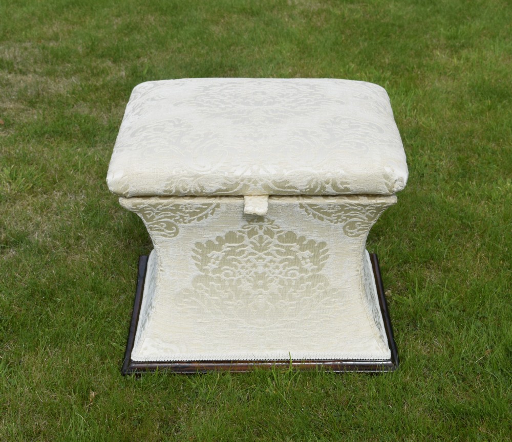 A square Regency storage ottoman with concave sides, upholstered in cream damask fabric and set upon a dark rosewood plinth base.