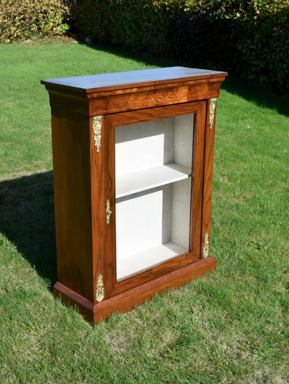 A Victorian warm brown walnut display cabinet featuring a single glazed door, floral wood inlay on the top frieze, and decorative brass mounts.