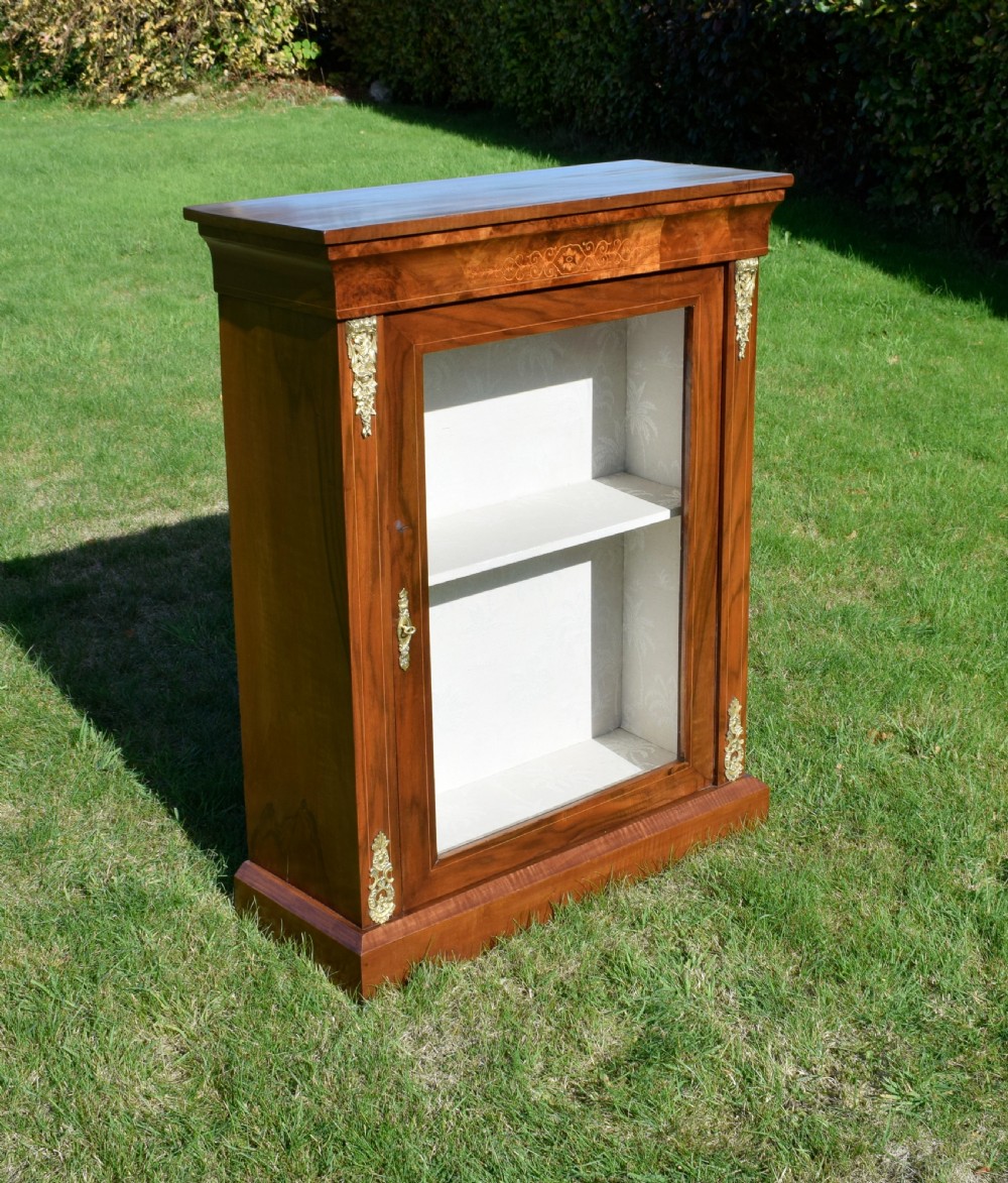A Victorian warm brown walnut display cabinet featuring a single glazed door, floral wood inlay on the top frieze, and decorative brass mounts. View II