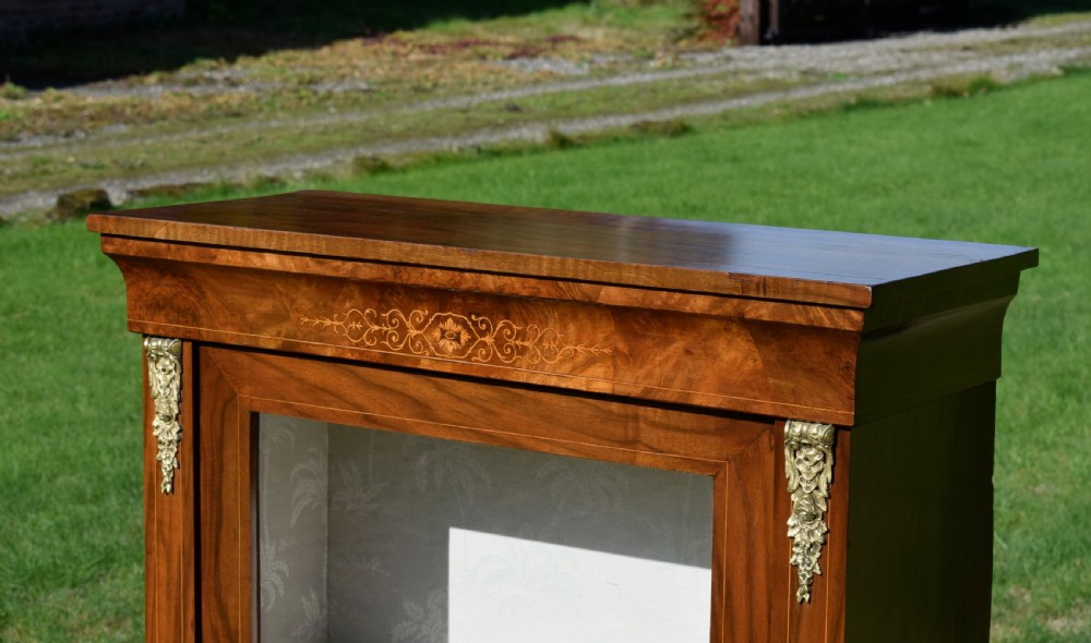 A Victorian warm brown walnut display cabinet featuring a single glazed door, floral wood inlay on the top frieze, and decorative brass mounts. View VII