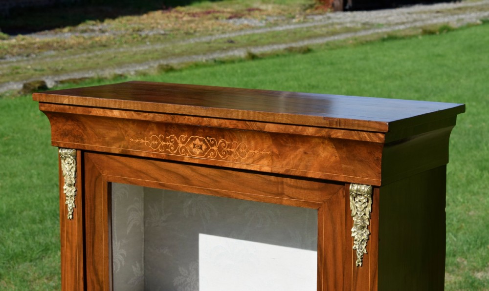 A Victorian warm brown walnut display cabinet featuring a single glazed door, floral wood inlay on the top frieze, and decorative brass mounts. View VIII