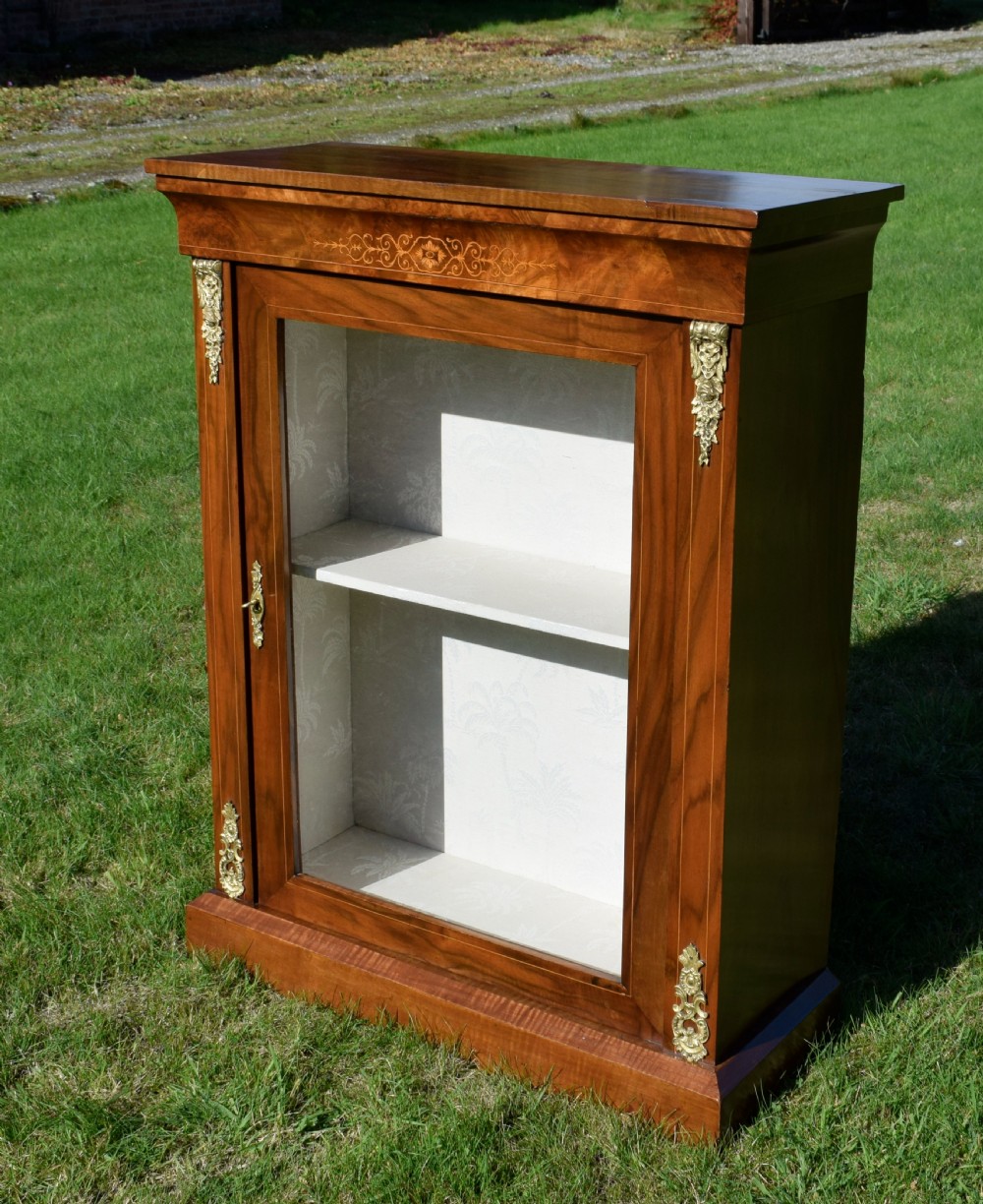 A Victorian warm brown walnut display cabinet featuring a single glazed door, floral wood inlay on the top frieze, and decorative brass mounts. View IX