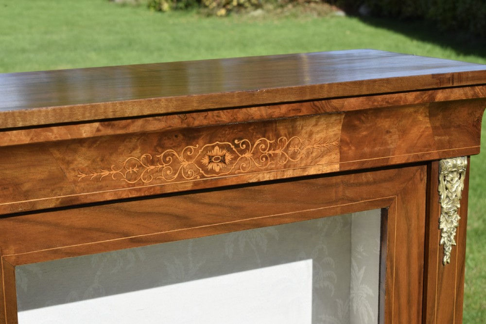 A Victorian warm brown walnut display cabinet featuring a single glazed door, floral wood inlay on the top frieze, and decorative brass mounts. View X