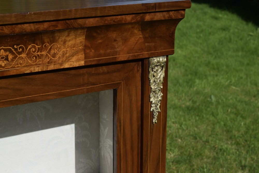 A Victorian warm brown walnut display cabinet featuring a single glazed door, floral wood inlay on the top frieze, and decorative brass mounts. View XI