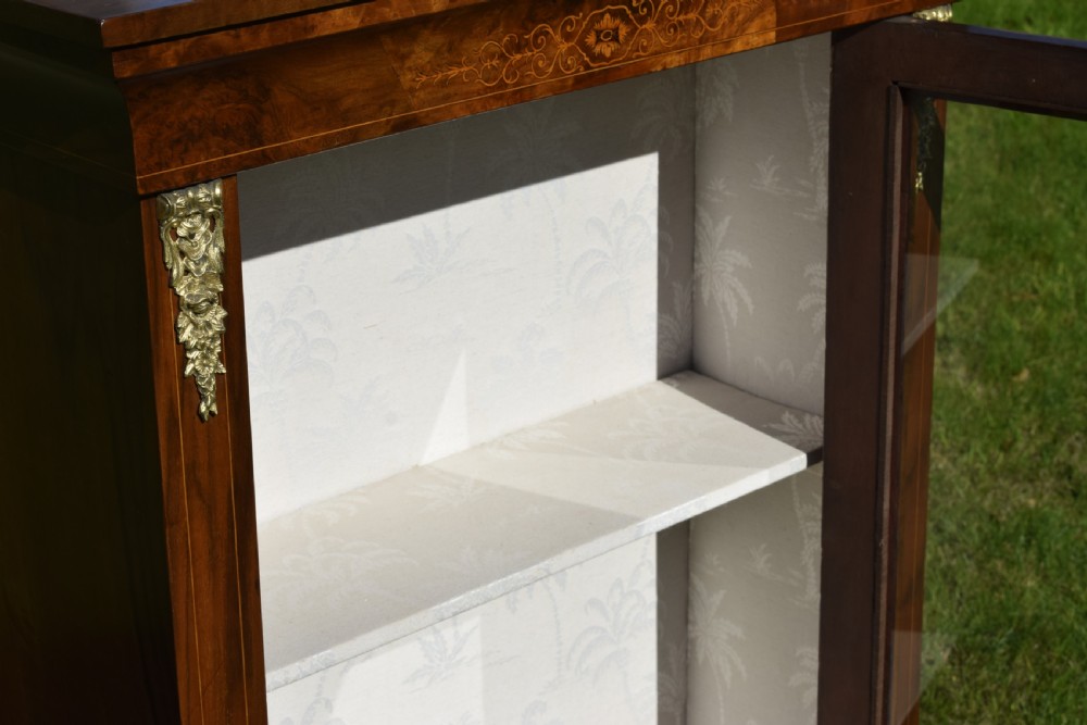 A Victorian warm brown walnut display cabinet featuring a single glazed door, floral wood inlay on the top frieze, and decorative brass mounts. View XII