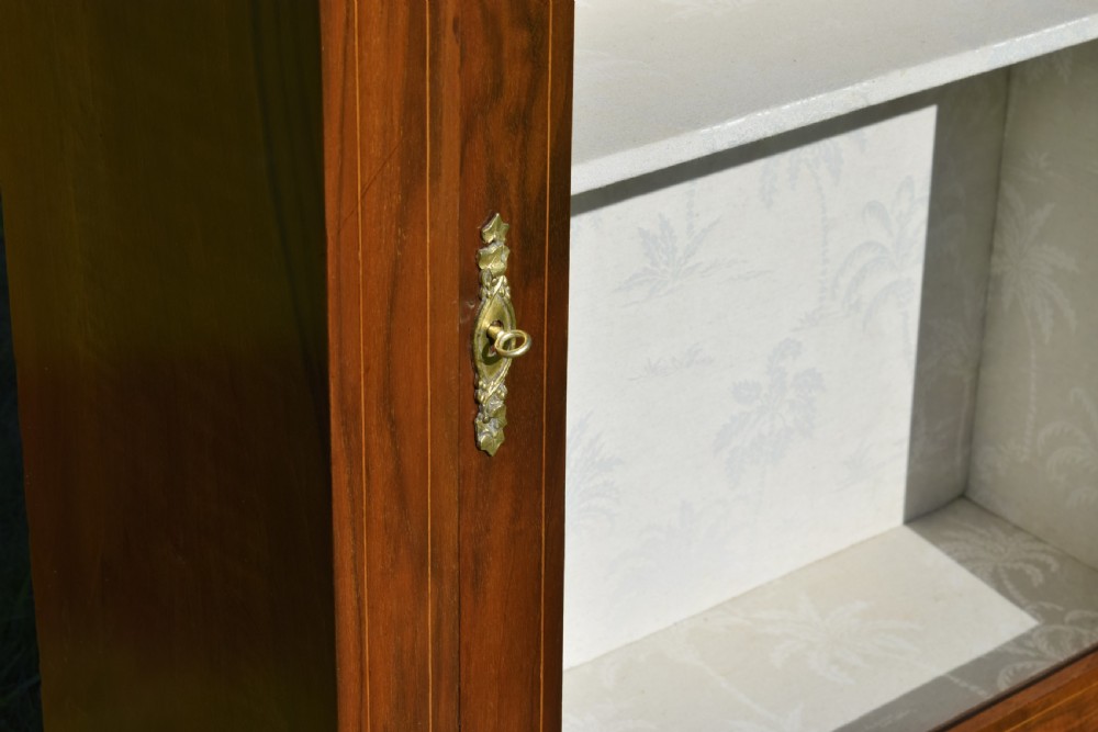 A Victorian warm brown walnut display cabinet featuring a single glazed door, floral wood inlay on the top frieze, and decorative brass mounts. View XIII