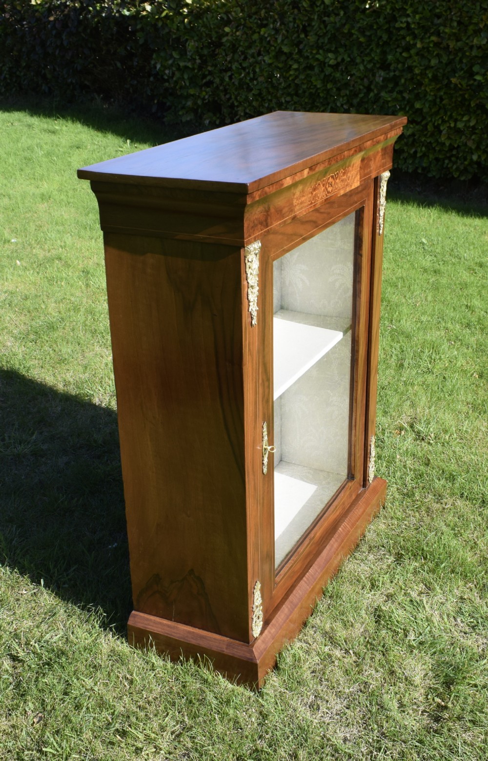 A Victorian warm brown walnut display cabinet featuring a single glazed door, floral wood inlay on the top frieze, and decorative brass mounts. View XIX