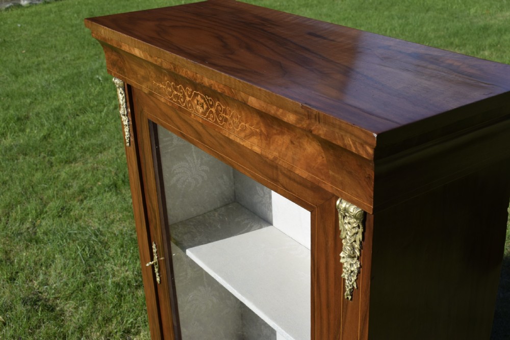 A Victorian warm brown walnut display cabinet featuring a single glazed door, floral wood inlay on the top frieze, and decorative brass mounts. View XX