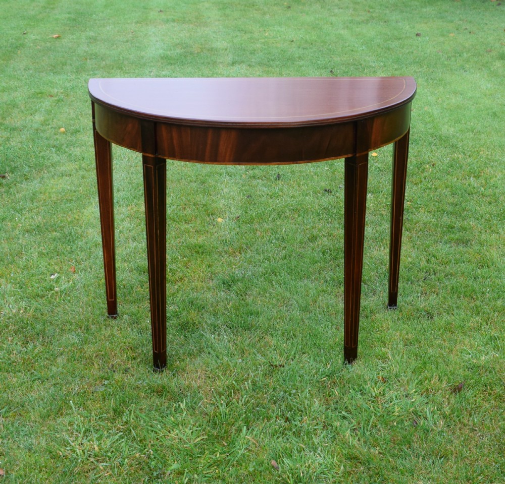 A mahogany demi-lune console table featuring light-coloured string inlay along the top perimeter, apron, and four square tapered legs. View III