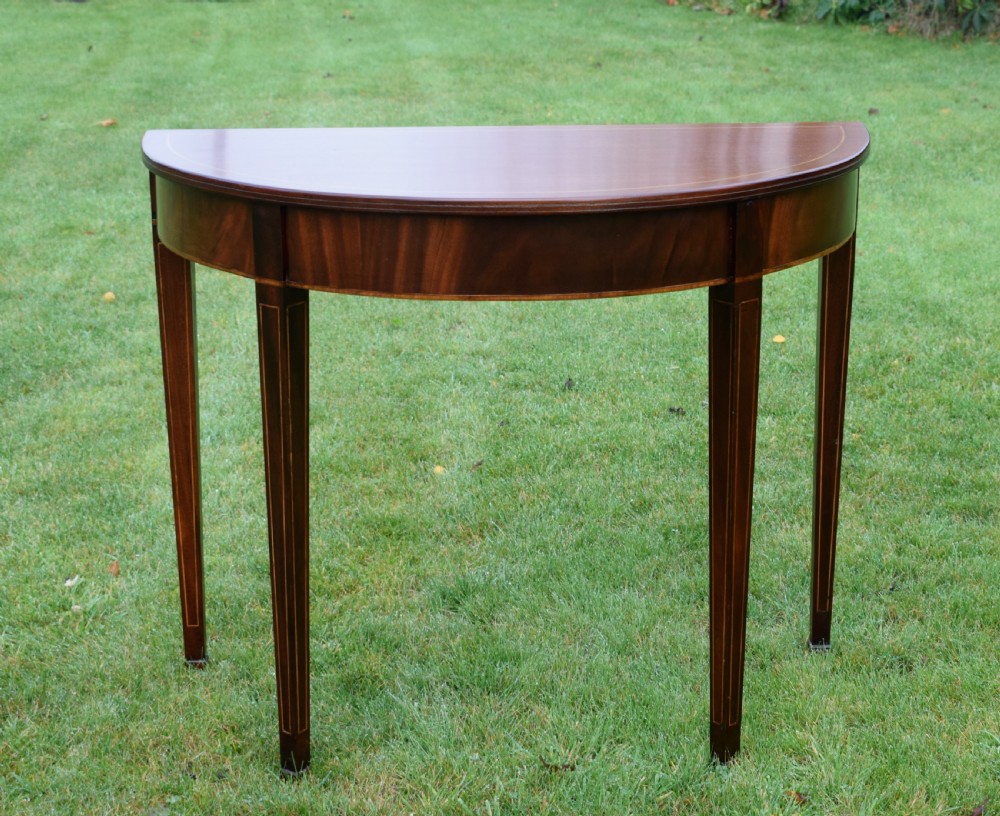 A mahogany demi-lune console table featuring light-coloured string inlay along the top perimeter, apron, and four square tapered legs. View V
