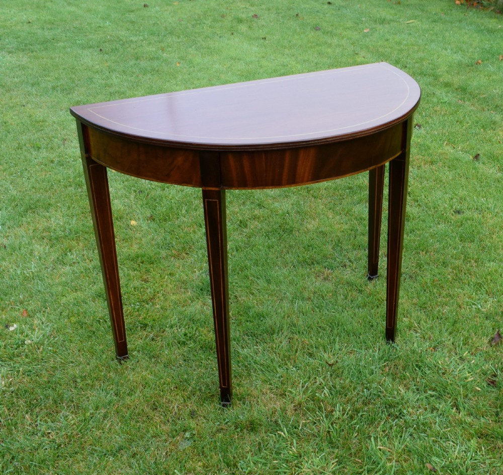 A mahogany demi-lune console table featuring light-coloured string inlay along the top perimeter, apron, and four square tapered legs. View VII