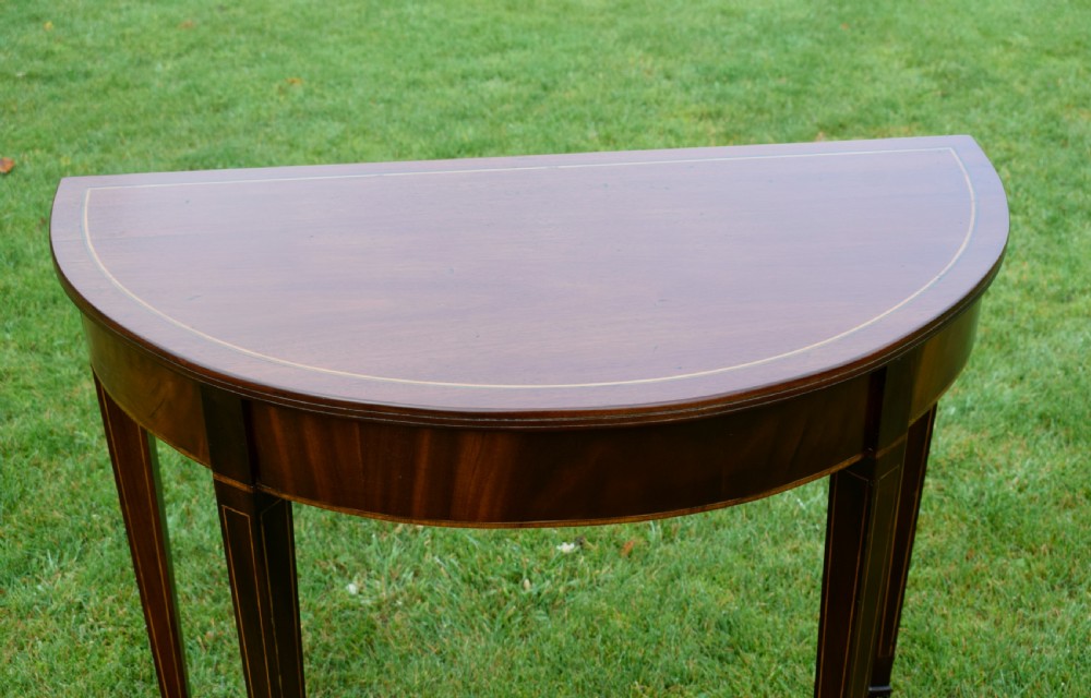 A mahogany demi-lune console table featuring light-coloured string inlay along the top perimeter, apron, and four square tapered legs. View VIII