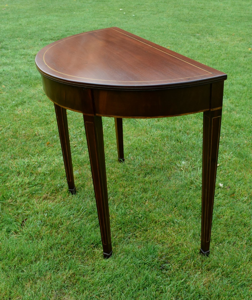 A mahogany demi-lune console table featuring light-coloured string inlay along the top perimeter, apron, and four square tapered legs. View IX