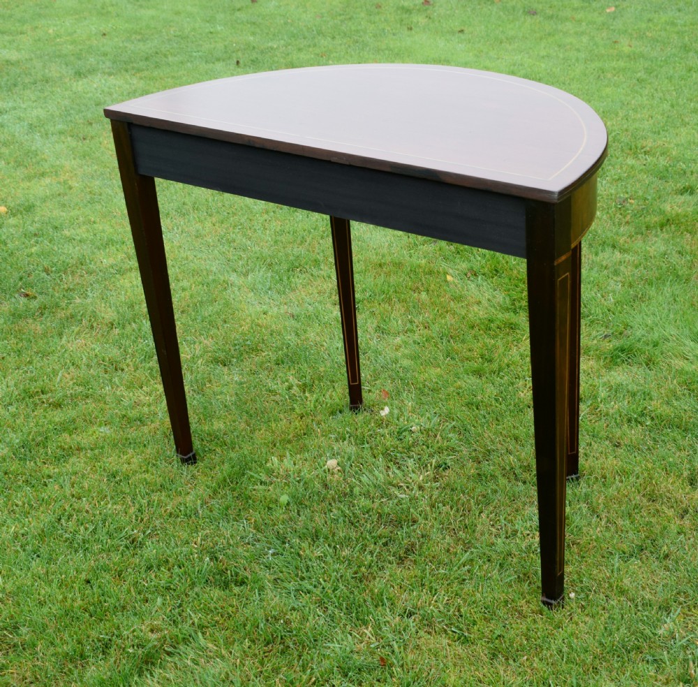 A mahogany demi-lune console table featuring light-coloured string inlay along the top perimeter, apron, and four square tapered legs. View XI
