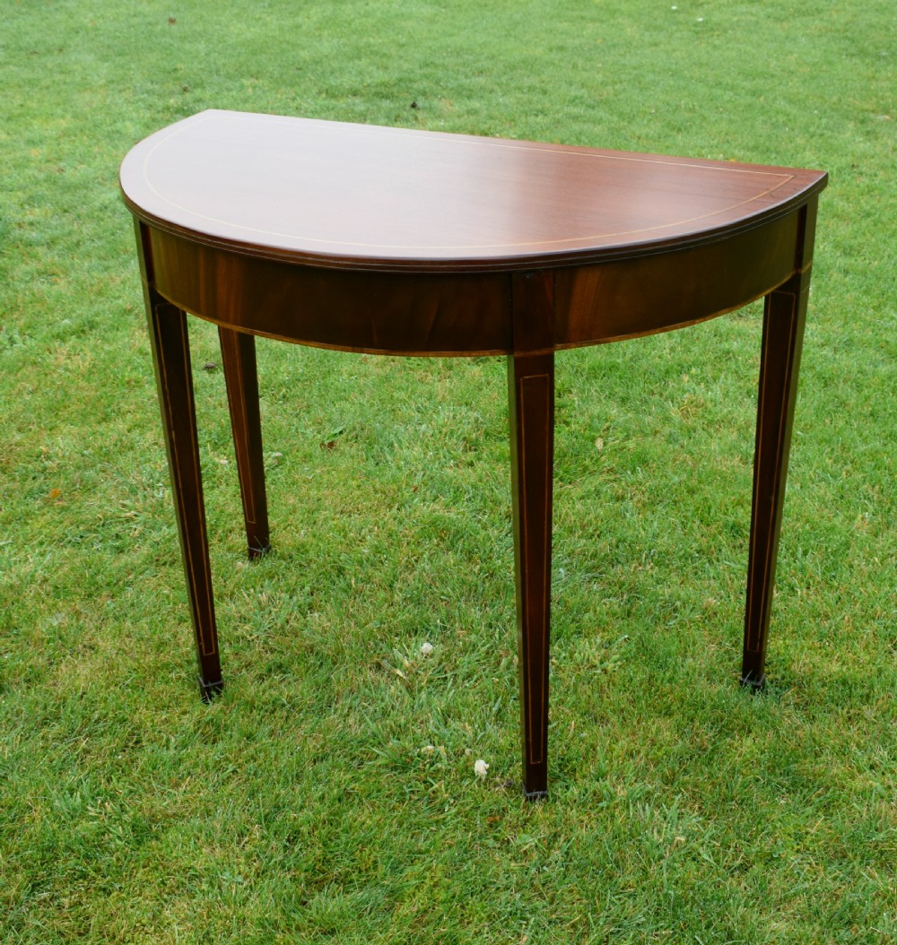 A mahogany demi-lune console table featuring light-coloured string inlay along the top perimeter, apron, and four square tapered legs. View XIII