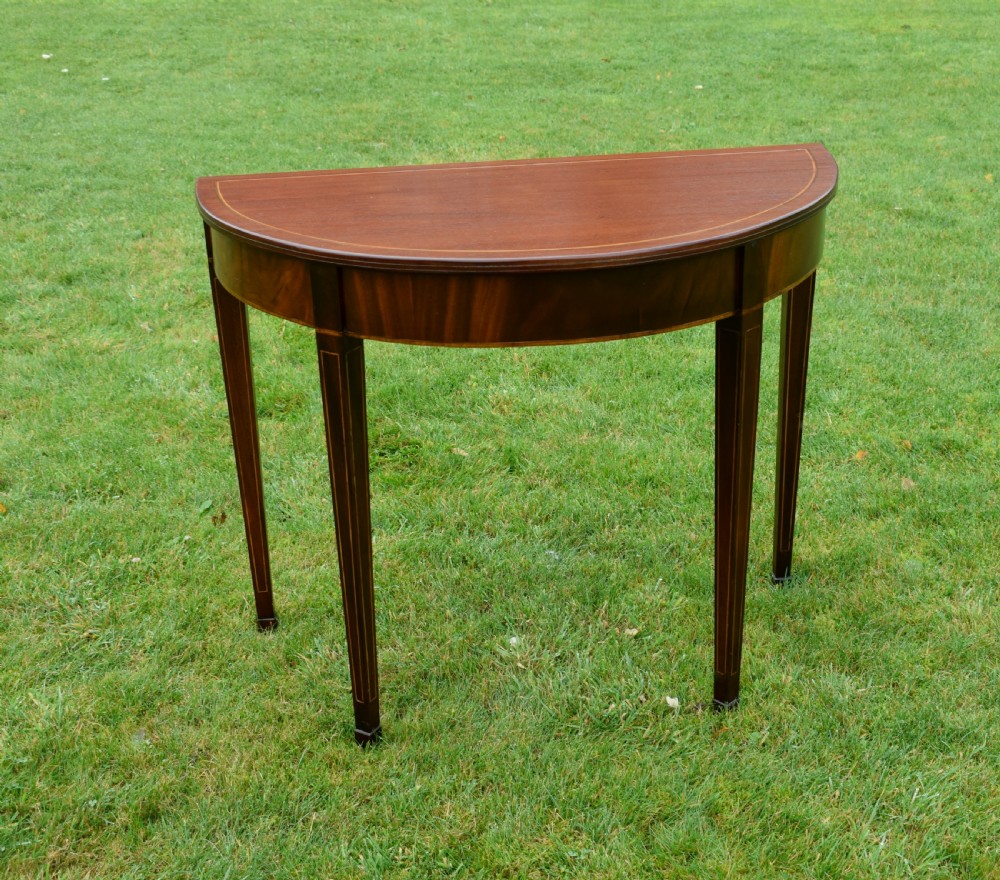 A mahogany demi-lune console table featuring light-coloured string inlay along the top perimeter, apron, and four square tapered legs. View XIV