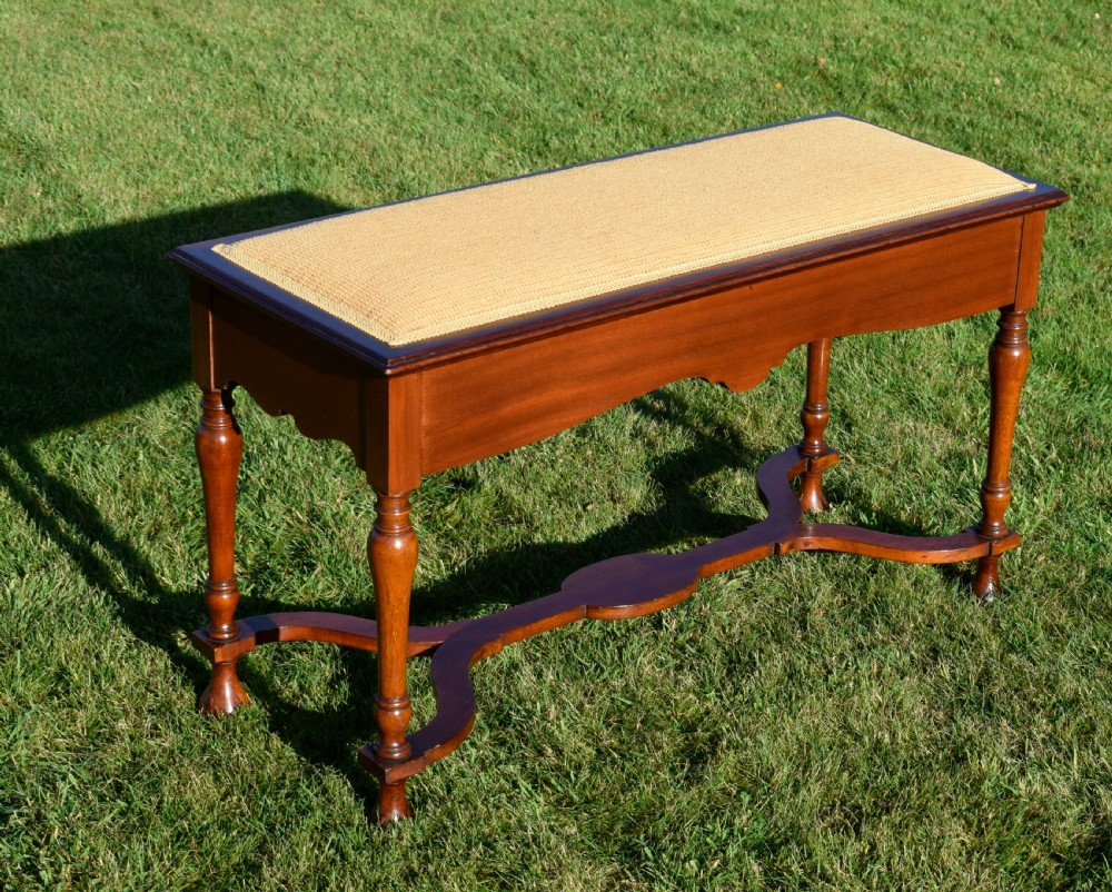 A long mahogany duet stool featuring turned legs, a shaped apron, a central curved cross-stretcher, and a yellow woven upholstered seat.