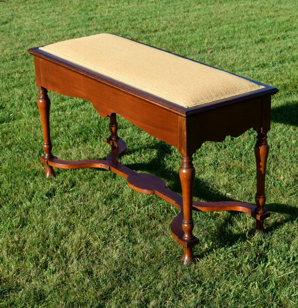 A long mahogany duet stool featuring turned legs, a shaped apron, a central curved cross-stretcher, and a yellow woven upholstered seat. View V