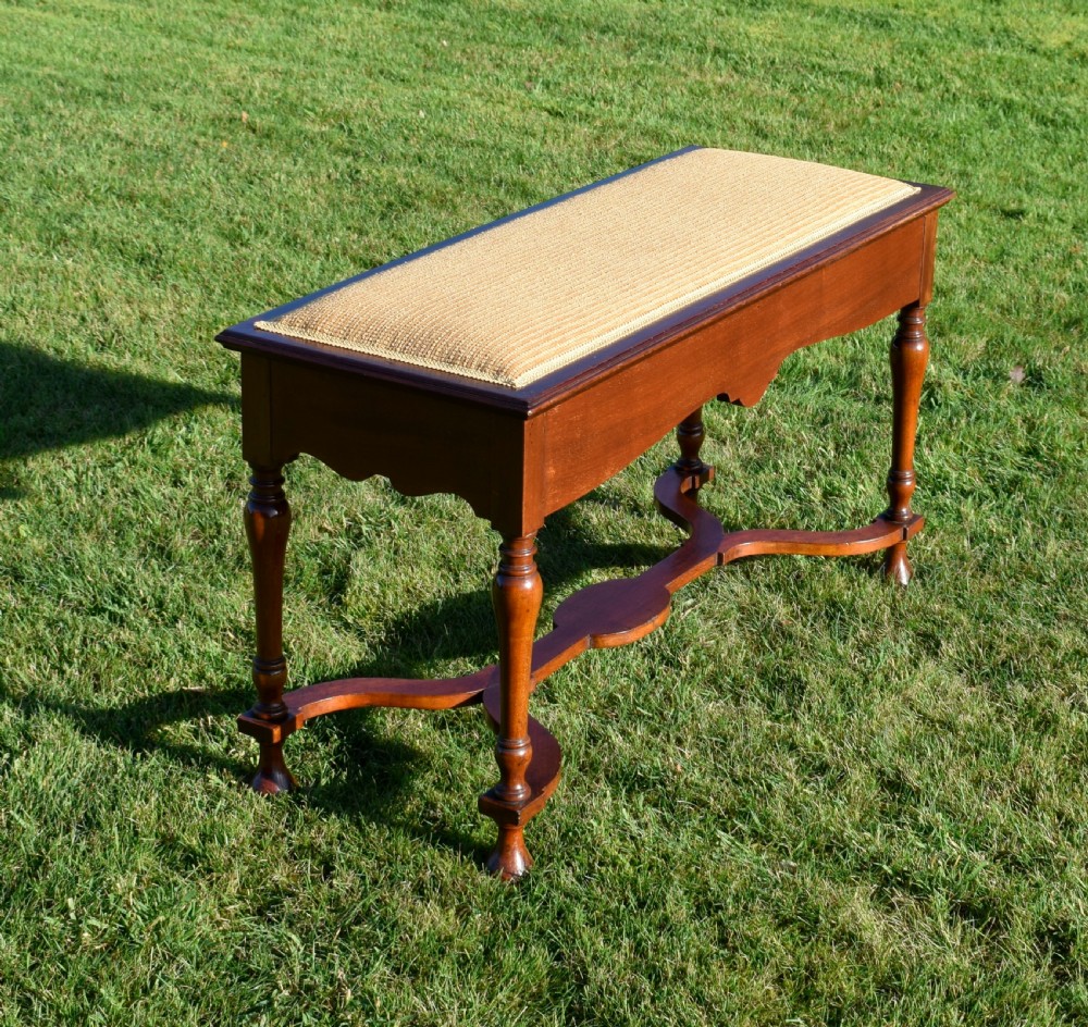 A long mahogany duet stool featuring turned legs, a shaped apron, a central curved cross-stretcher, and a yellow woven upholstered seat. View VII