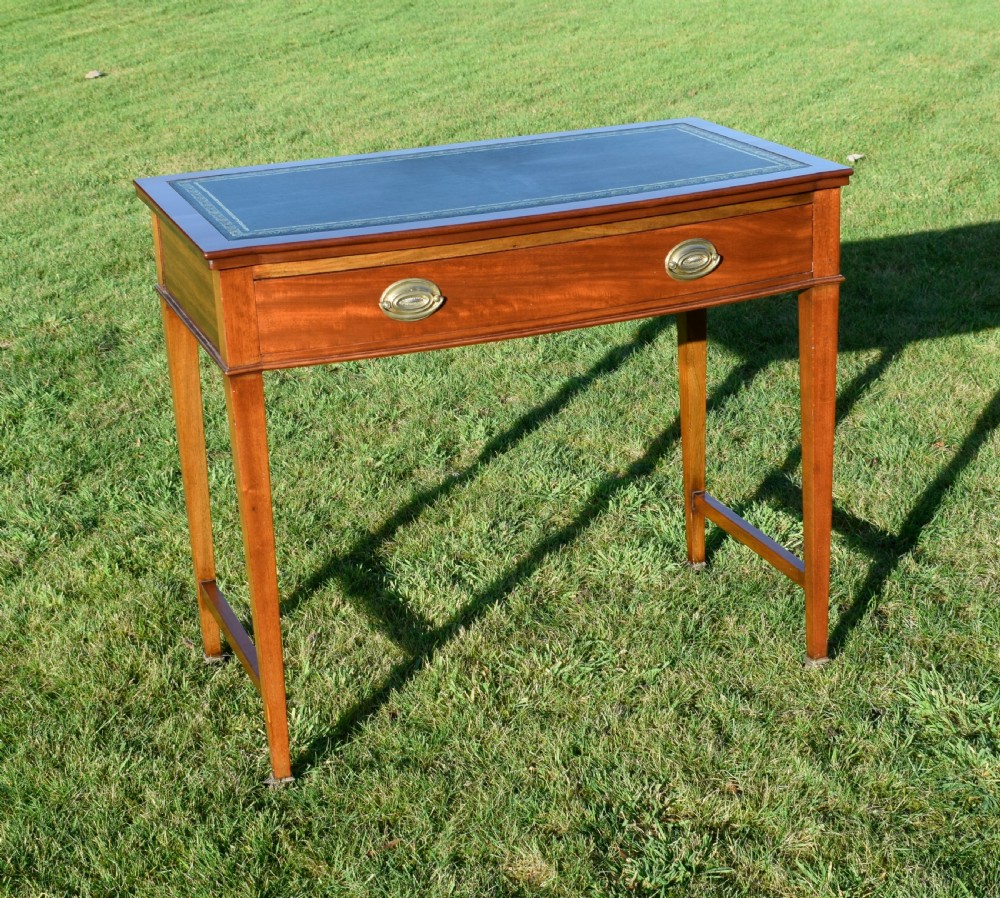 An early twentieth-century mahogany writing table featuring an inset green leather top, a single drawer with two brass oval drop handles, and tapered square legs.