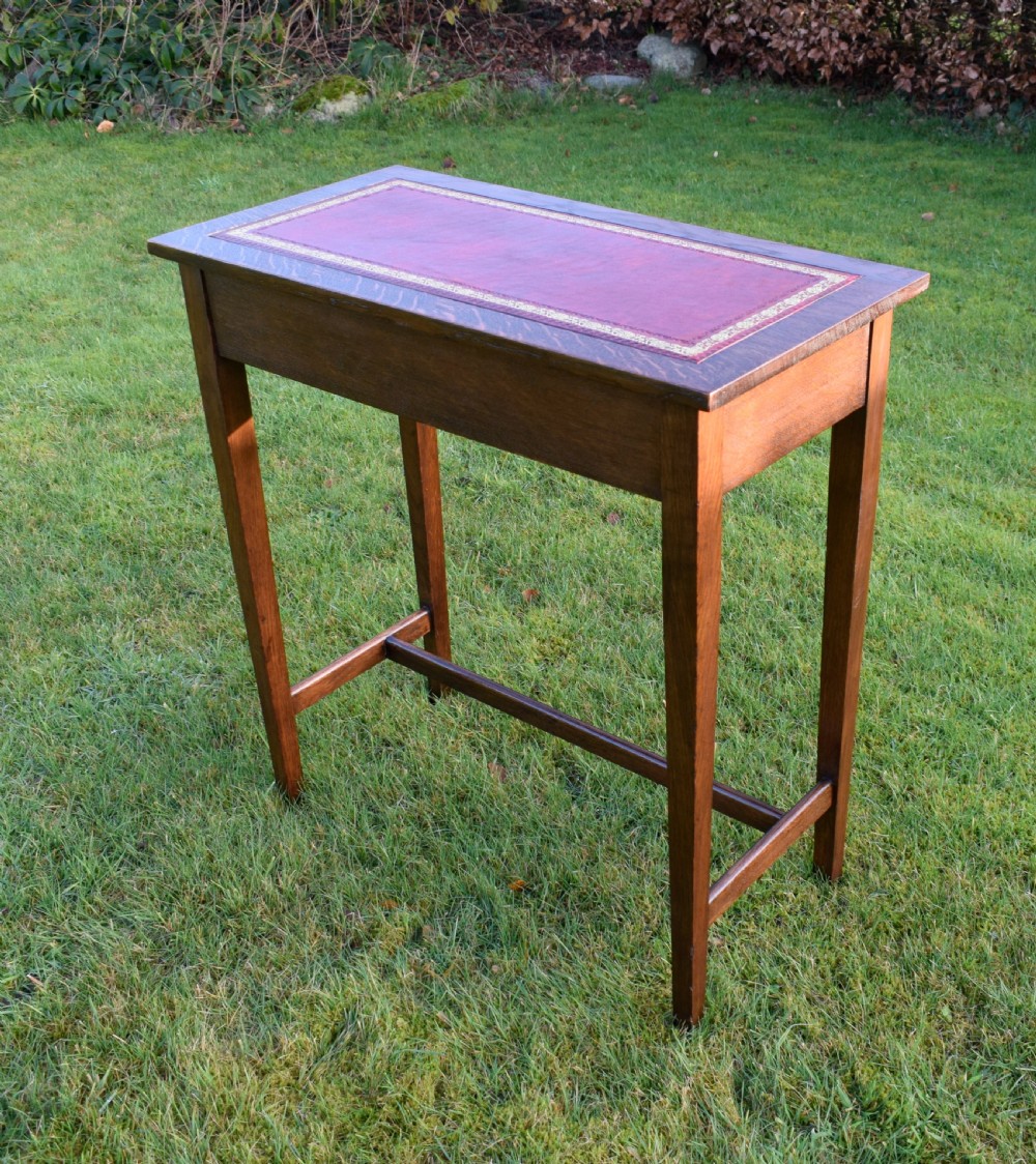 A rectangular Arts and Crafts oak writing table featuring a burgundy leather inset top with gold tooling and a lower H-stretcher.