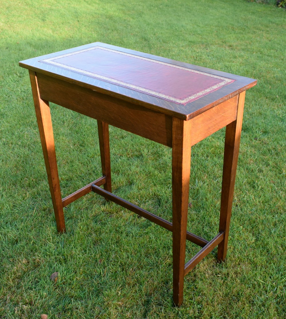 A rectangular Arts and Crafts oak writing table featuring a burgundy leather inset top with gold tooling and a lower H-stretcher. View III