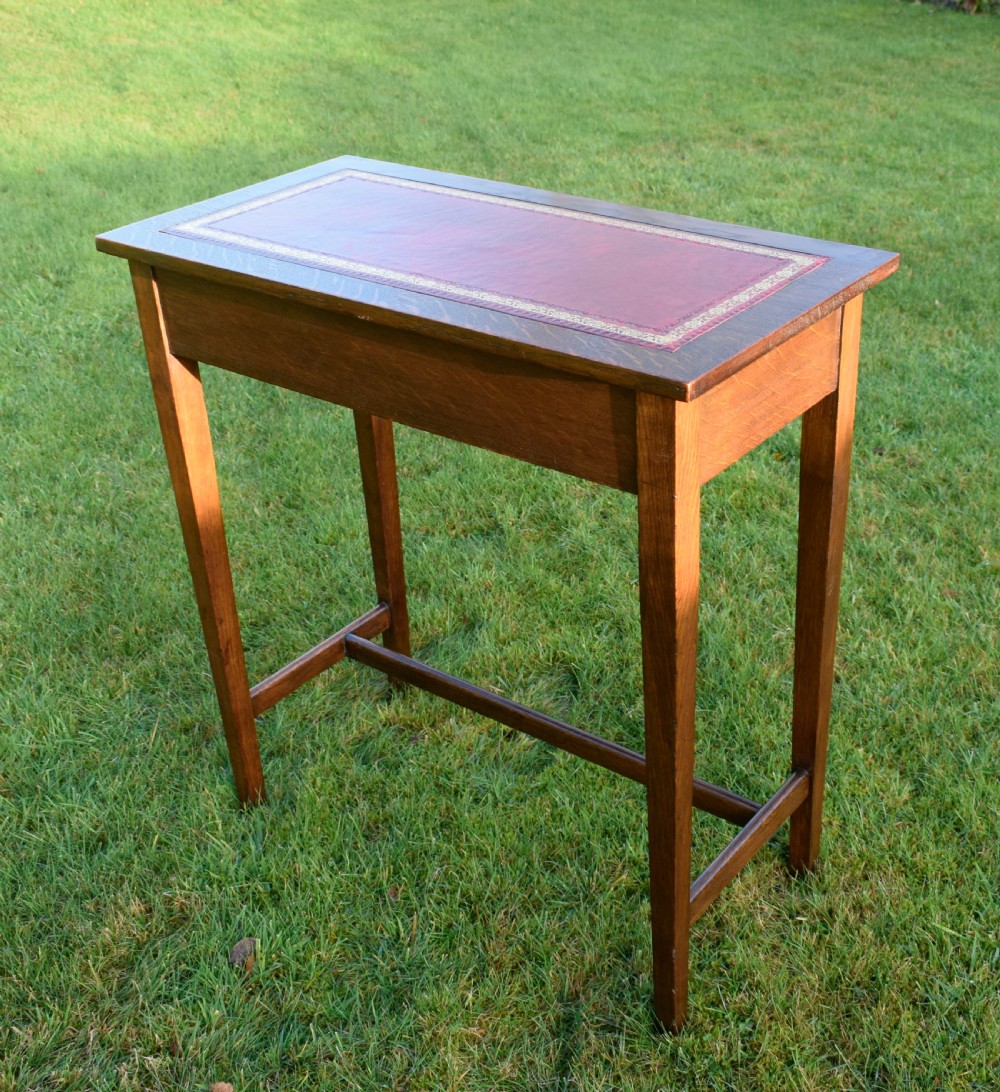 A rectangular Arts and Crafts oak writing table featuring a burgundy leather inset top with gold tooling and a lower H-stretcher. View IV