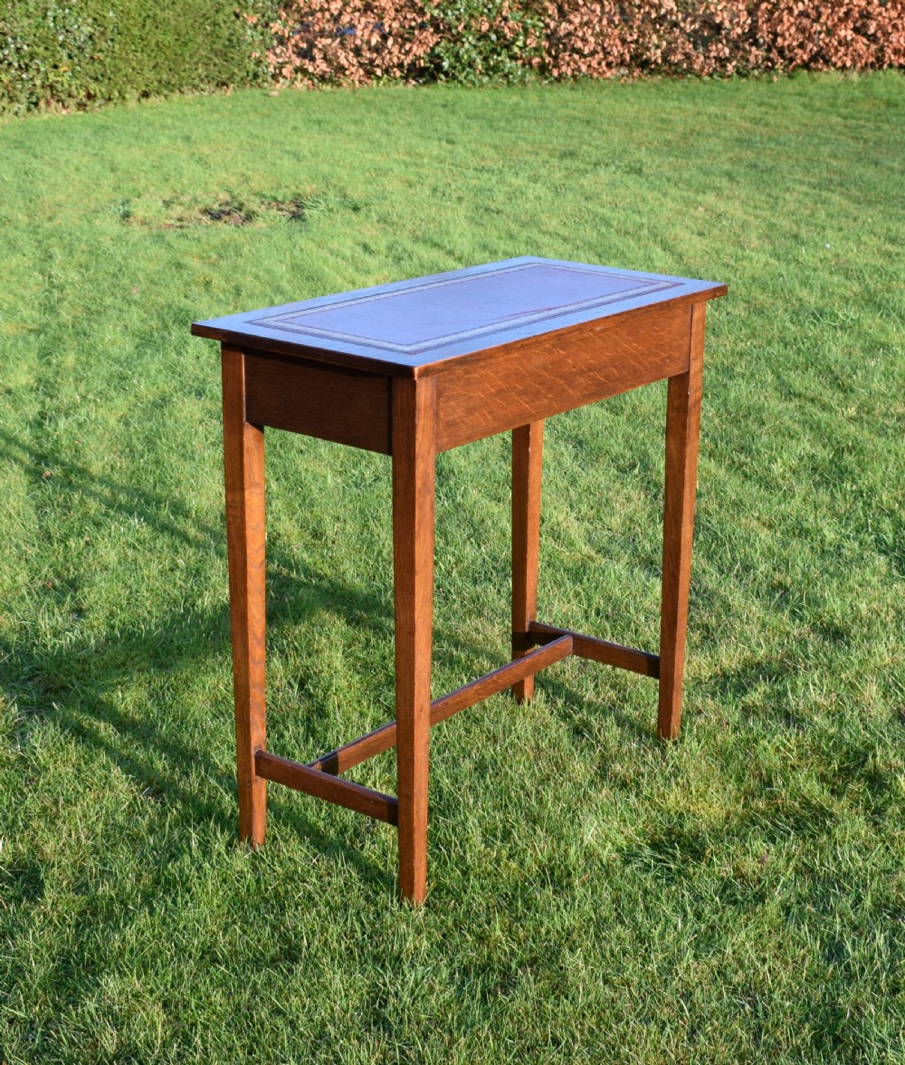 A rectangular Arts and Crafts oak writing table featuring a burgundy leather inset top with gold tooling and a lower H-stretcher. View V