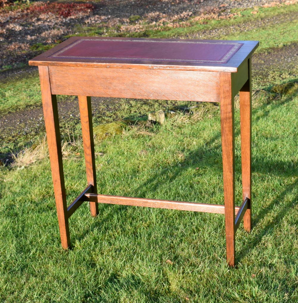 A rectangular Arts and Crafts oak writing table featuring a burgundy leather inset top with gold tooling and a lower H-stretcher. View VI