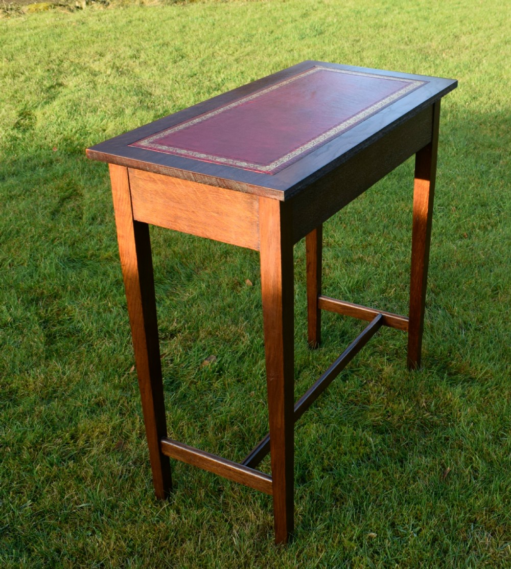 A rectangular Arts and Crafts oak writing table featuring a burgundy leather inset top with gold tooling and a lower H-stretcher. View VII