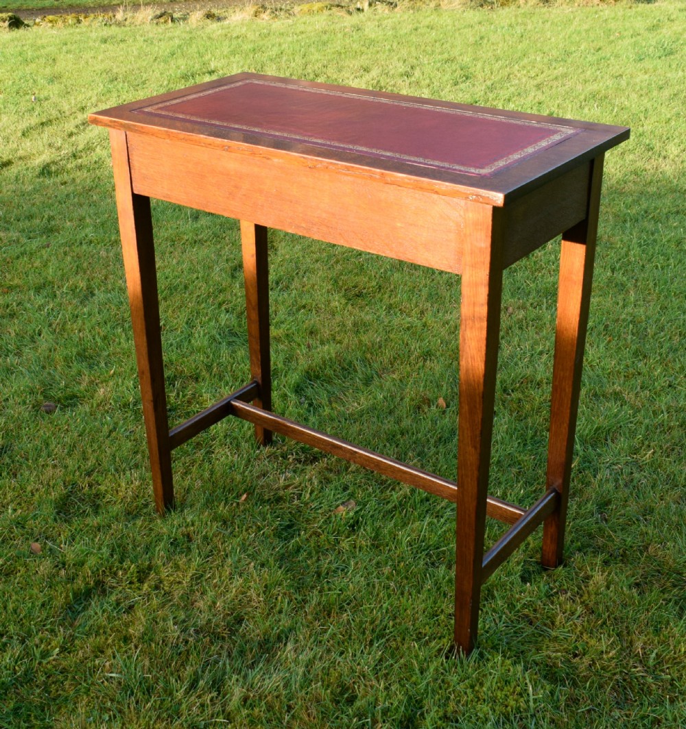 A rectangular Arts and Crafts oak writing table featuring a burgundy leather inset top with gold tooling and a lower H-stretcher. View VIII