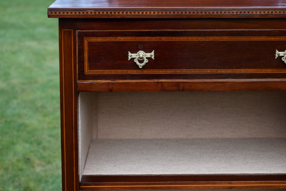An Edwardian inlaid mahogany display cabinet featuring a shaped upstand gallery, a single top drawer with brass drop handles, and a glass-fronted door opening to fabric-lined interior shelves. View VI
