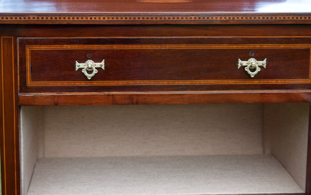 An Edwardian inlaid mahogany display cabinet featuring a shaped upstand gallery, a single top drawer with brass drop handles, and a glass-fronted door opening to fabric-lined interior shelves. View XII