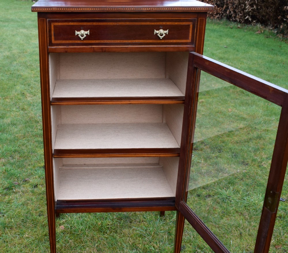 An Edwardian inlaid mahogany display cabinet featuring a shaped upstand gallery, a single top drawer with brass drop handles, and a glass-fronted door opening to fabric-lined interior shelves. View XIV