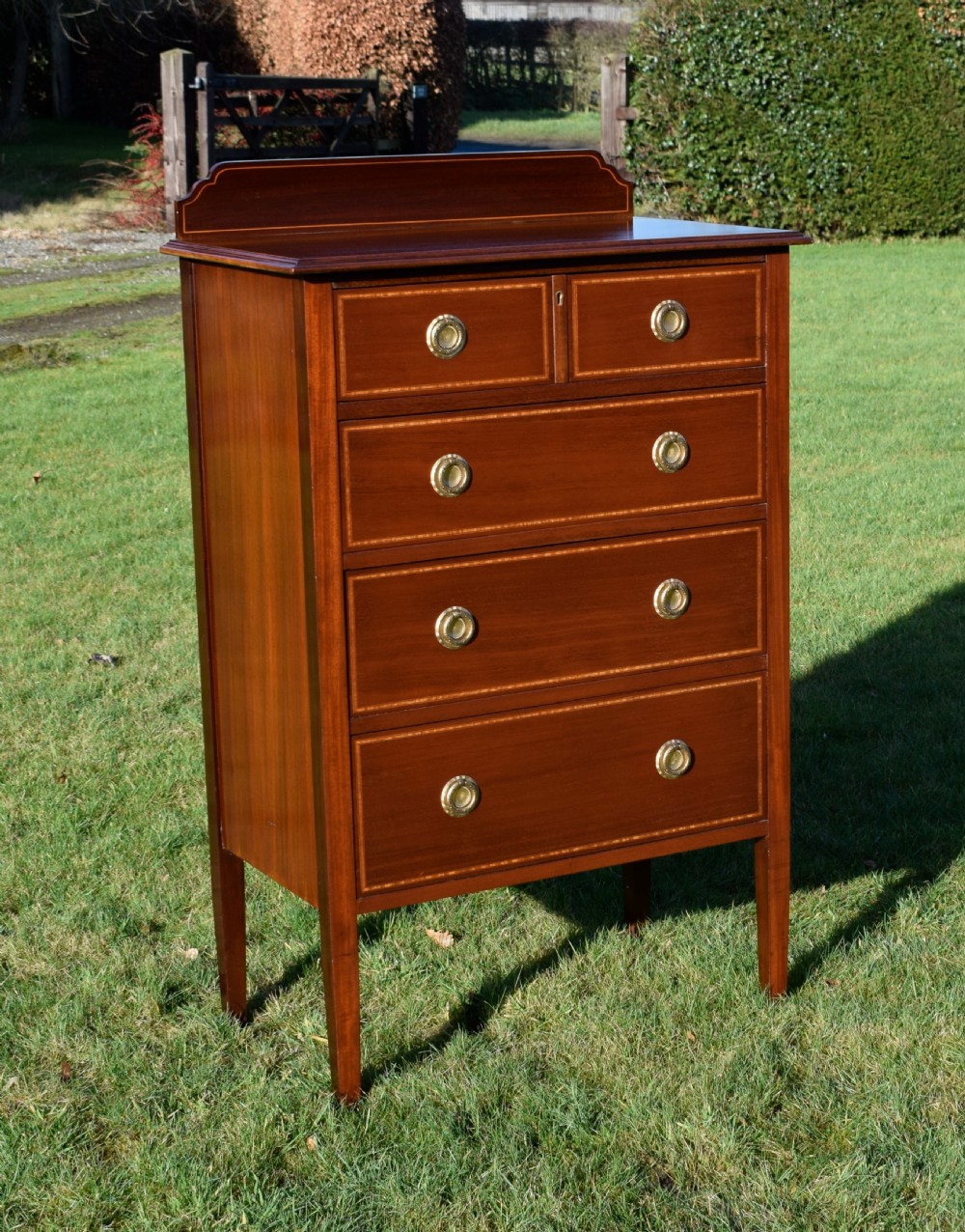 An Edwardian mahogany tall chest of drawers featuring fine string inlay, brass ring handles, five drawers, a low raised backboard, and square tapered legs. View II