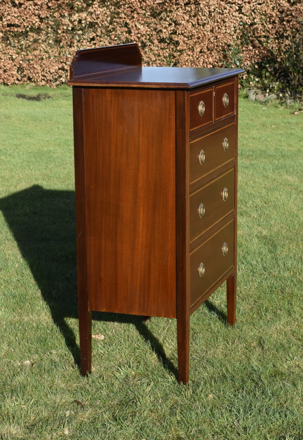 An Edwardian mahogany tall chest of drawers featuring fine string inlay, brass ring handles, five drawers, a low raised backboard, and square tapered legs. View IV