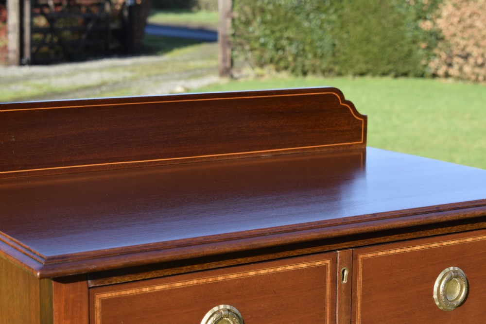 An Edwardian mahogany tall chest of drawers featuring fine string inlay, brass ring handles, five drawers, a low raised backboard, and square tapered legs. View VI