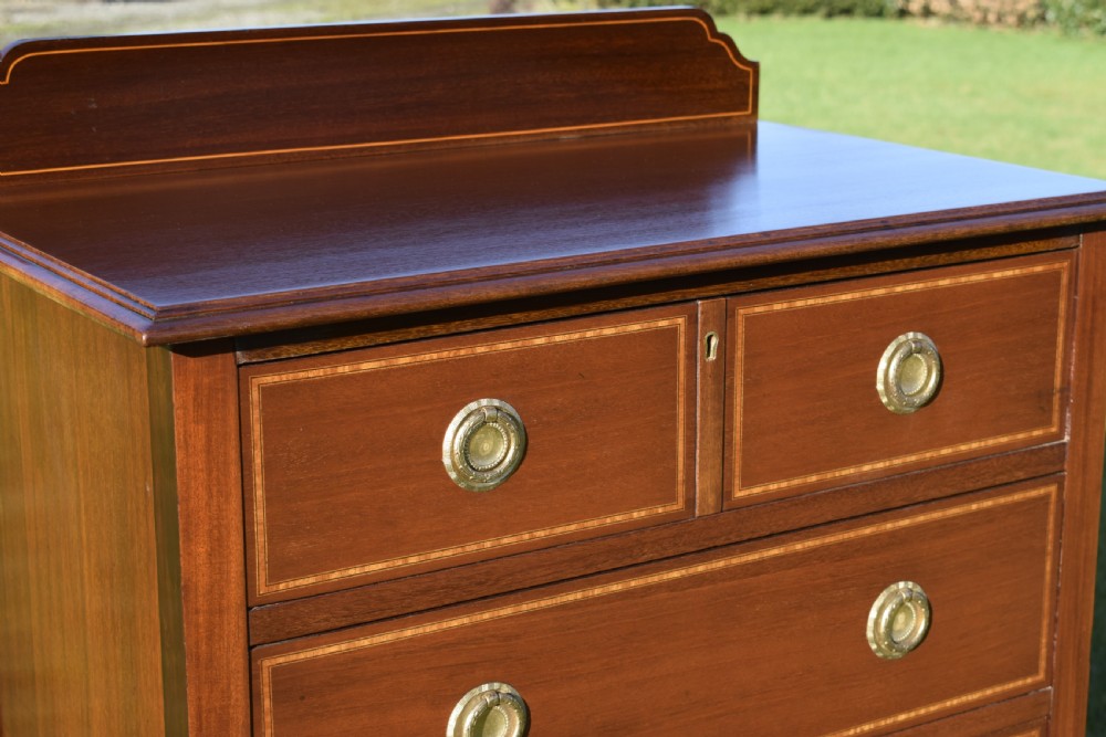 An Edwardian mahogany tall chest of drawers featuring fine string inlay, brass ring handles, five drawers, a low raised backboard, and square tapered legs. View VII