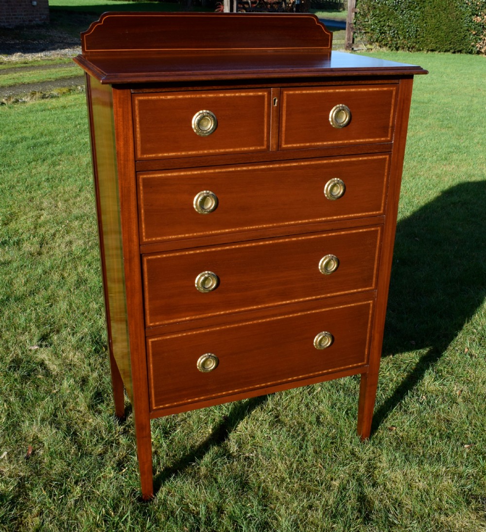An Edwardian mahogany tall chest of drawers featuring fine string inlay, brass ring handles, five drawers, a low raised backboard, and square tapered legs. View VIII