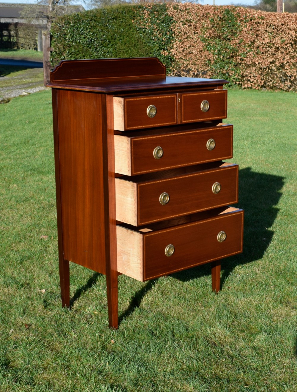 An Edwardian mahogany tall chest of drawers featuring fine string inlay, brass ring handles, five drawers, a low raised backboard, and square tapered legs. View X