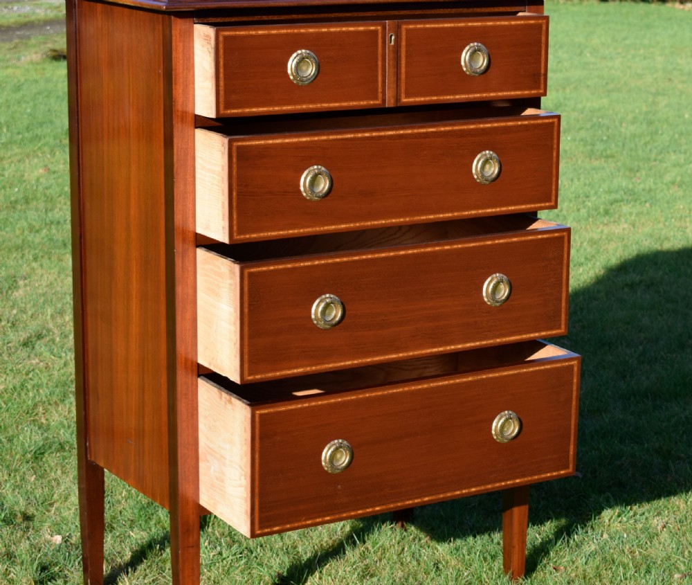 An Edwardian mahogany tall chest of drawers featuring fine string inlay, brass ring handles, five drawers, a low raised backboard, and square tapered legs. View XI
