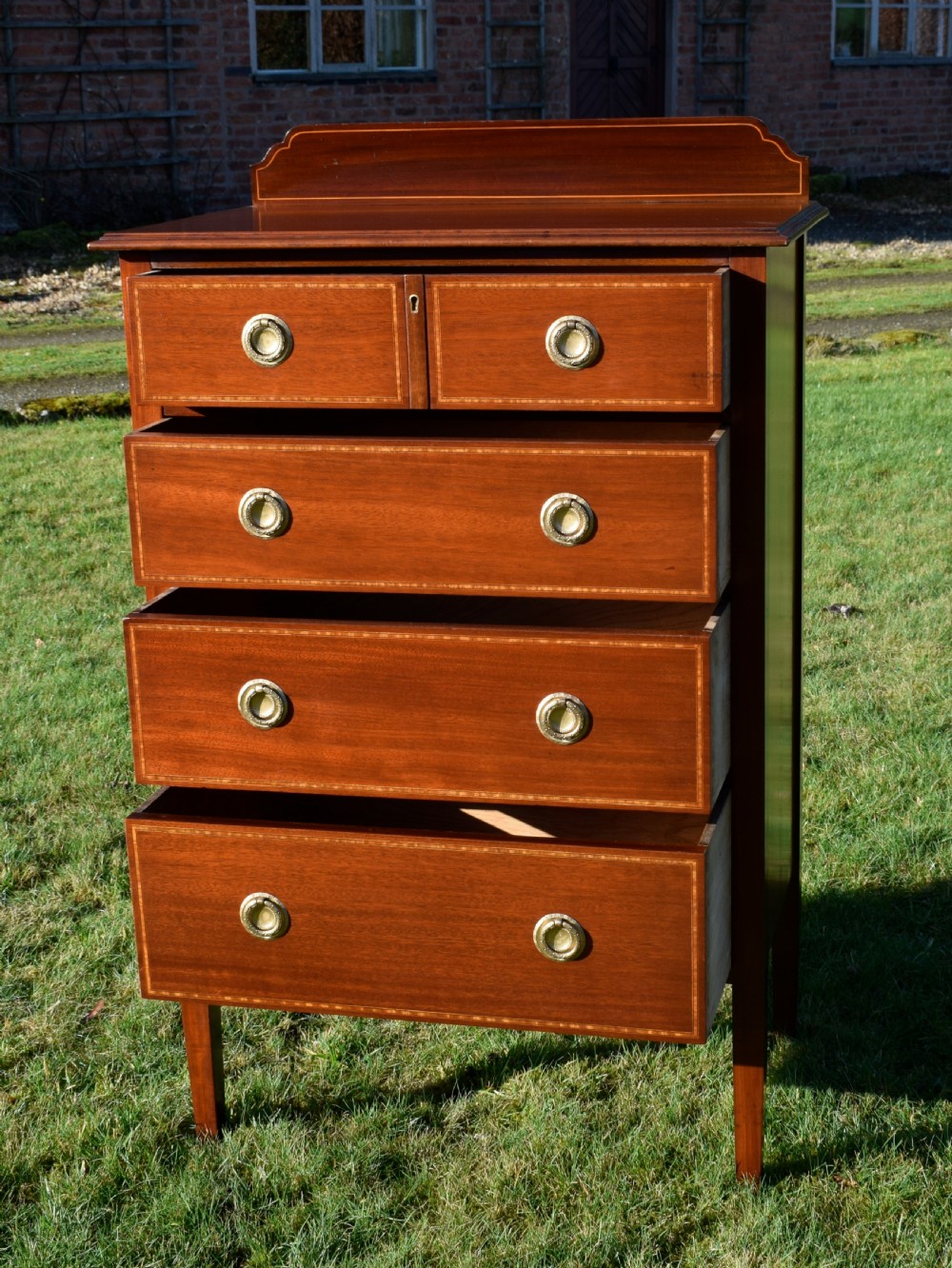 An Edwardian mahogany tall chest of drawers featuring fine string inlay, brass ring handles, five drawers, a low raised backboard, and square tapered legs. View XII
